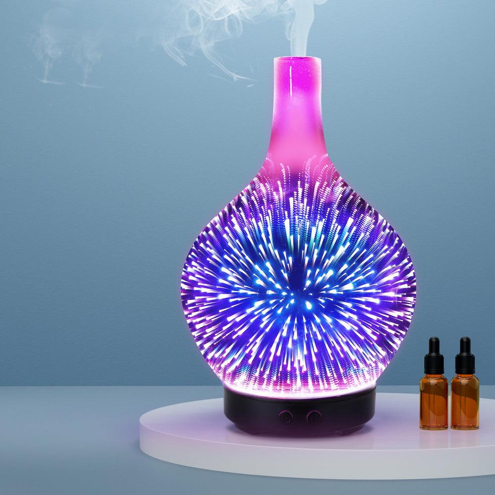 Glass aroma diffuser with 3D LED light pattern and essential oil bottles on a white tray